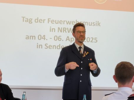 Detlef Budde spricht vor einer Präsentation zum Tag der Feuerwehrmusik.